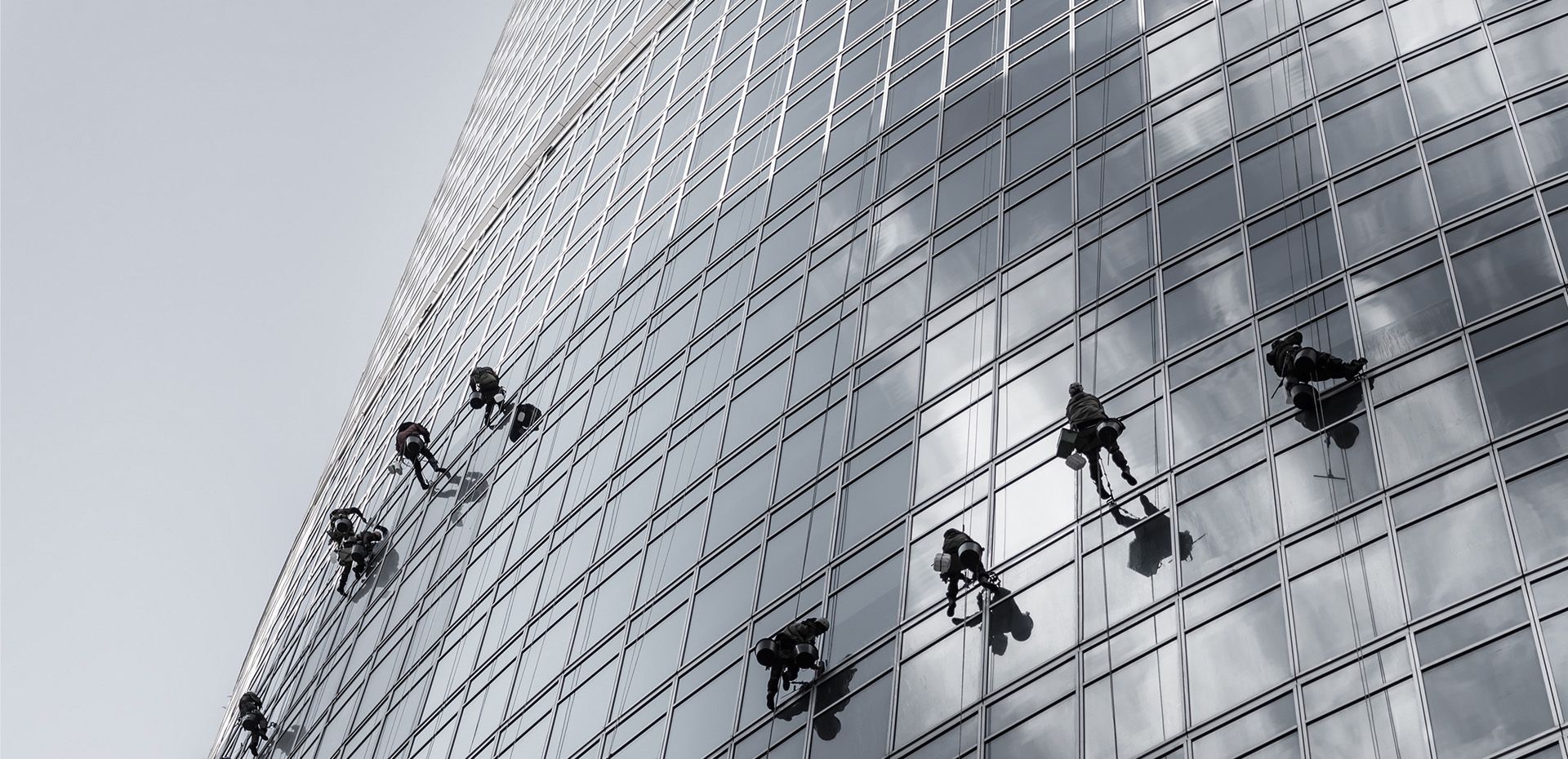 Menschen reinigen Fenster an der Seite eines Gebäudes mit professionellen Ausrüstungen und Sicherheitsvorkehrungen.