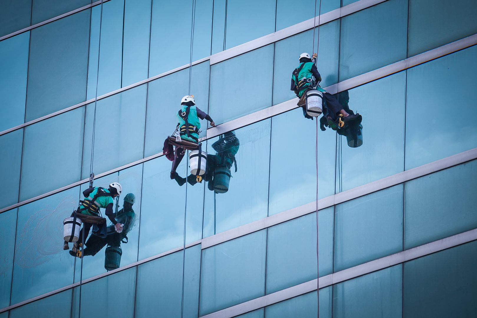 Drei Männer in Sicherheitsausrüstung reinigen Fenster an einem Gebäude.